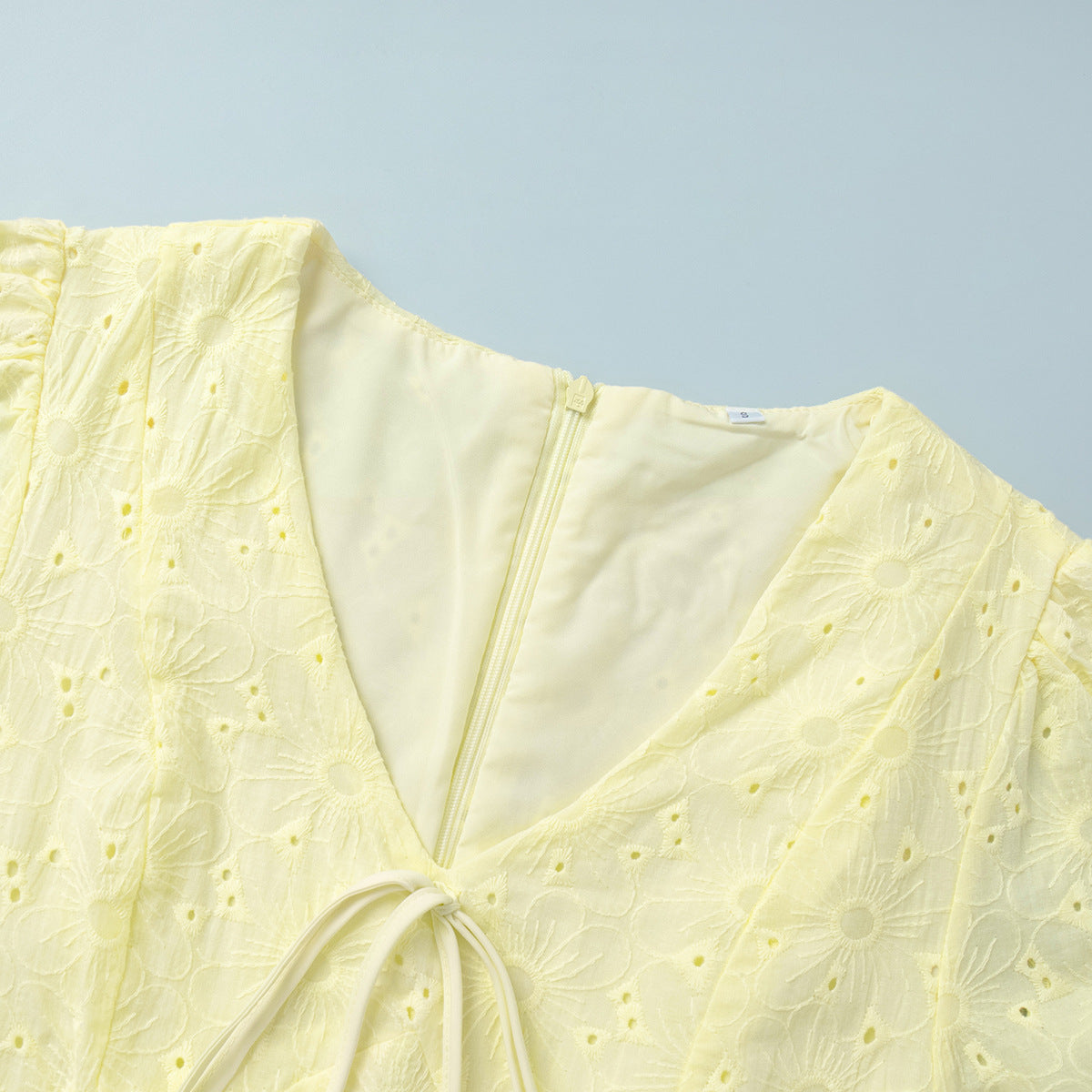 Yellow Eyelet Puff-Sleeve Mini Dress in Pale Yellow — close-up of the front tie