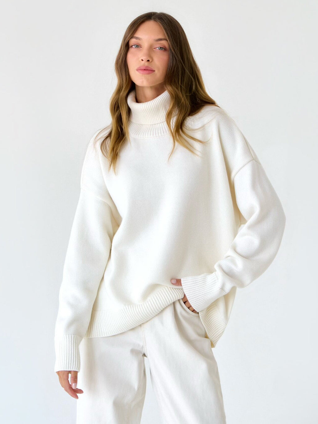 Oversized Knit Turtleneck Sweater in Ivory — on model with white trousers