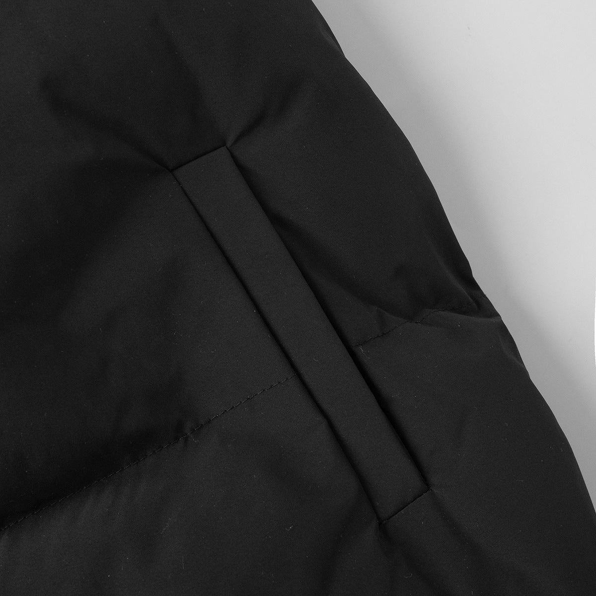 Longline Puffer Vest with High Stand Collar in Black — close-up of the side welt pocket