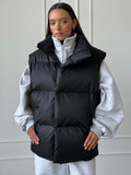 Longline Puffer Vest with High Stand Collar in Black — front view on model over a gray hoodie